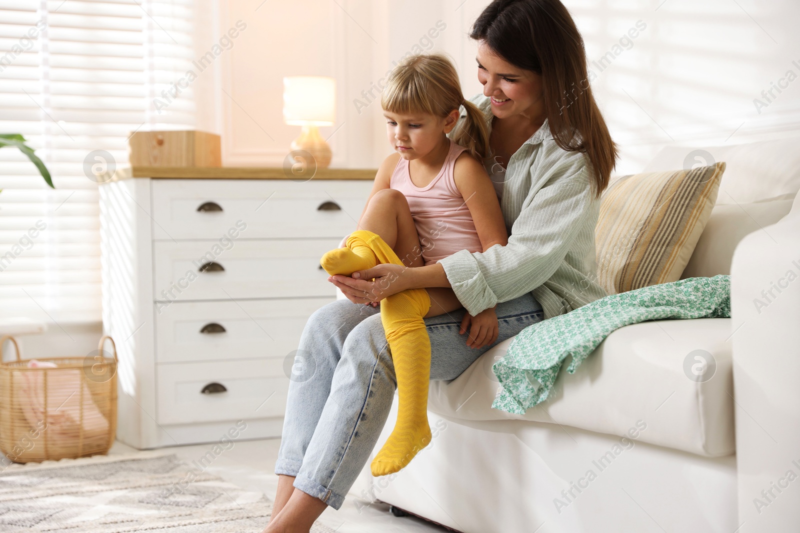 Photo of Mother helping her daughter to put tights on at home. Space for text