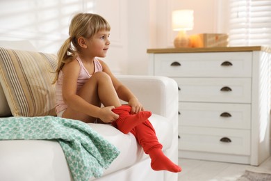 Photo of Little girl putting on soft tights at home. Space for text