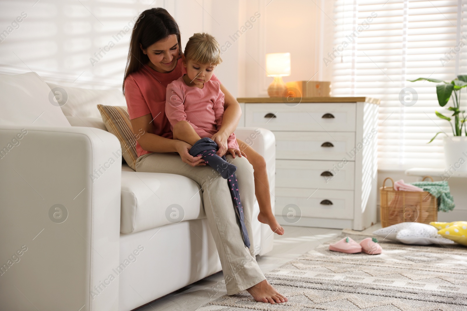 Photo of Mother helping her daughter to put tights on at home. Space for text