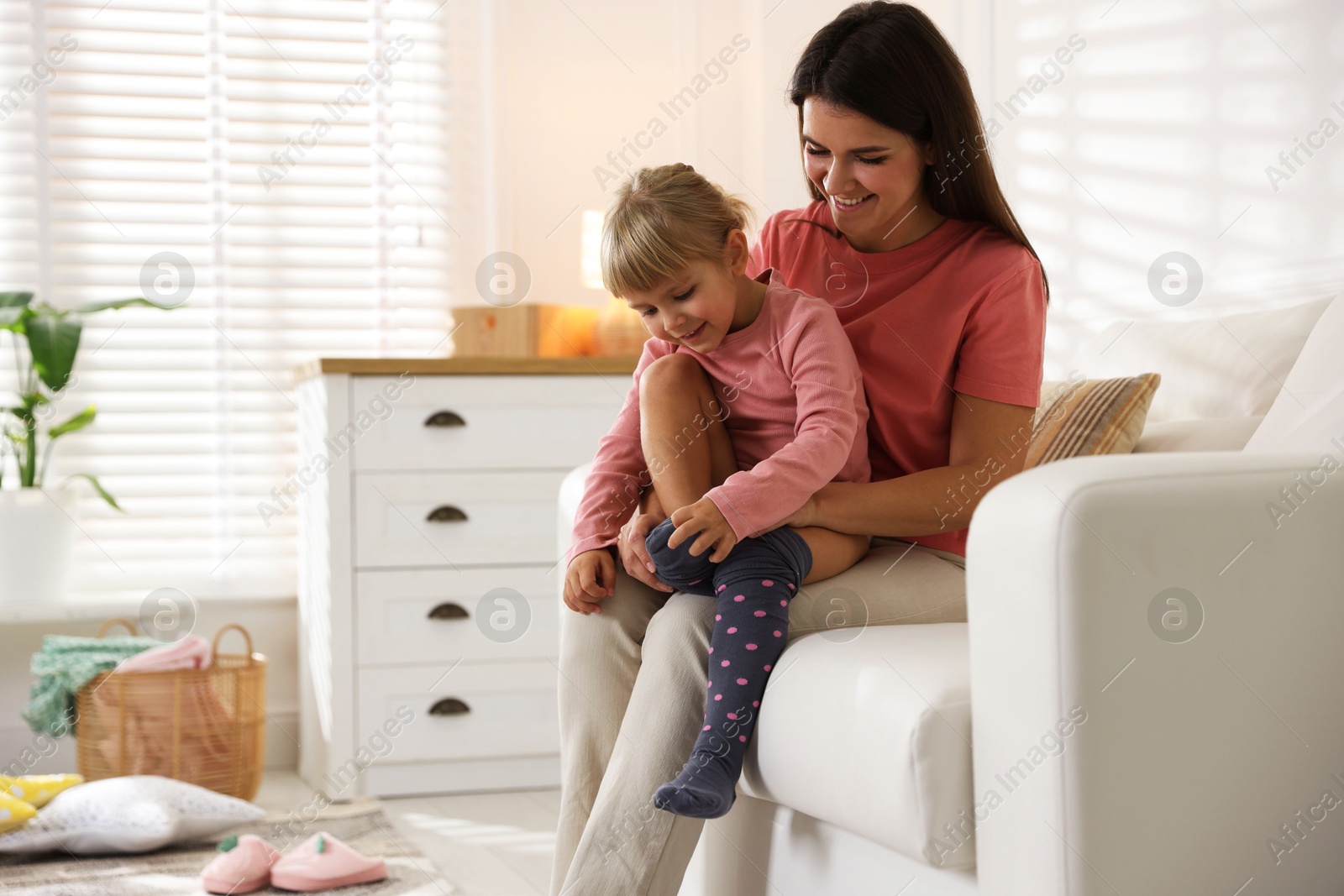 Photo of Mother helping her daughter to put tights on at home. Space for text