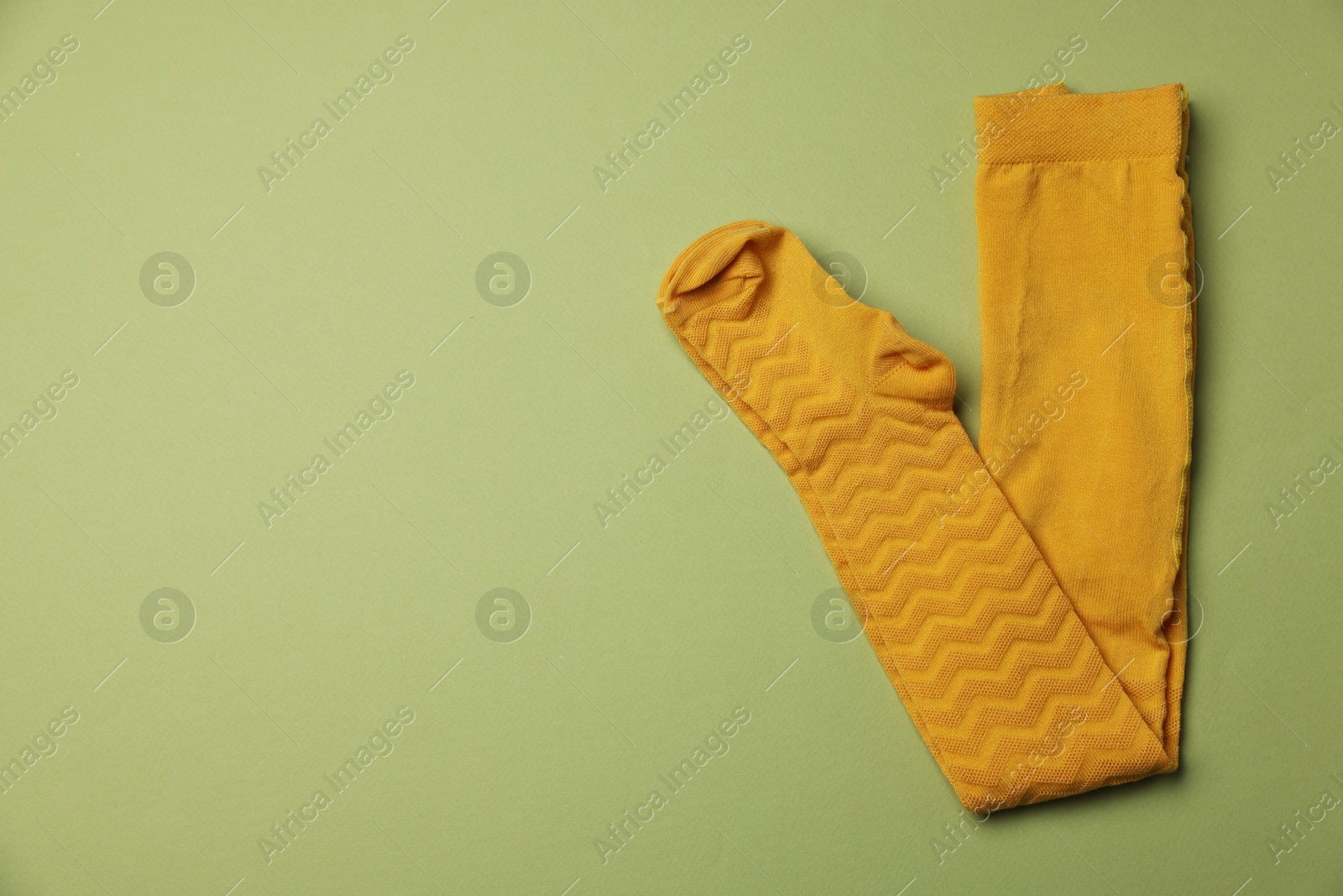 Photo of Beautiful yellow child's tights on green background, top view. Space for text