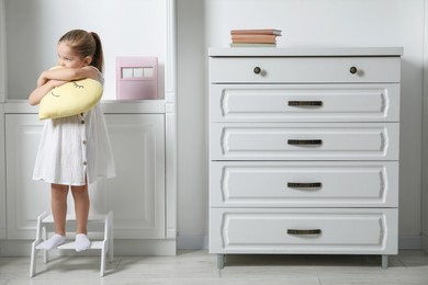 Photo of Little girl with toy standing on step stool indoors, space for text