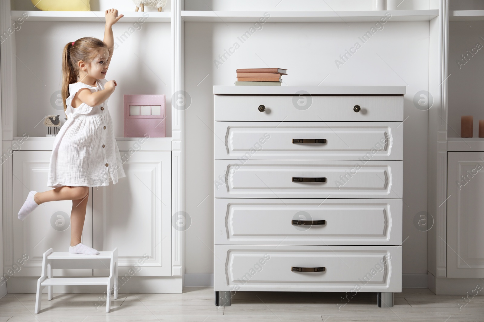 Photo of Little girl standing on step stool indoors, space for text