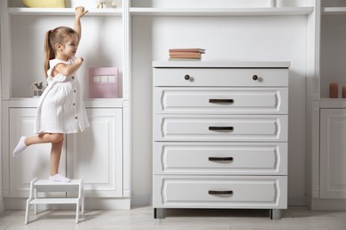 Photo of Little girl standing on step stool indoors, space for text