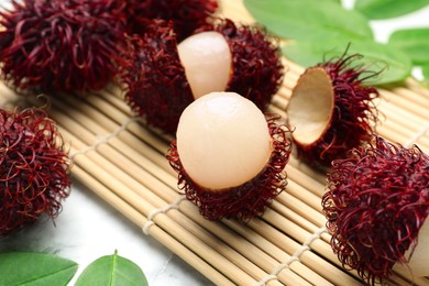 Photo of Delicious ripe rambutans and green leaves on white marble table, closeup