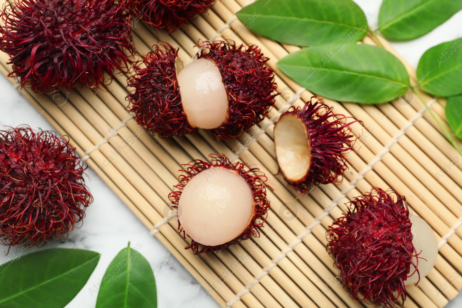 Photo of Delicious ripe rambutans and green leaves on white marble table, flat lay