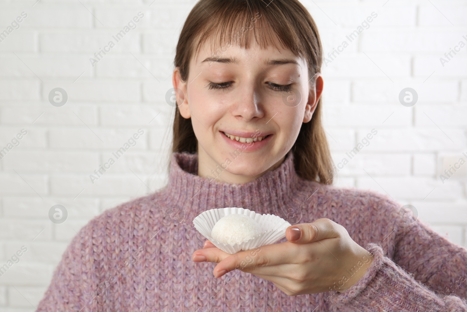 Photo of Smiling woman with tasty mochi near white wall