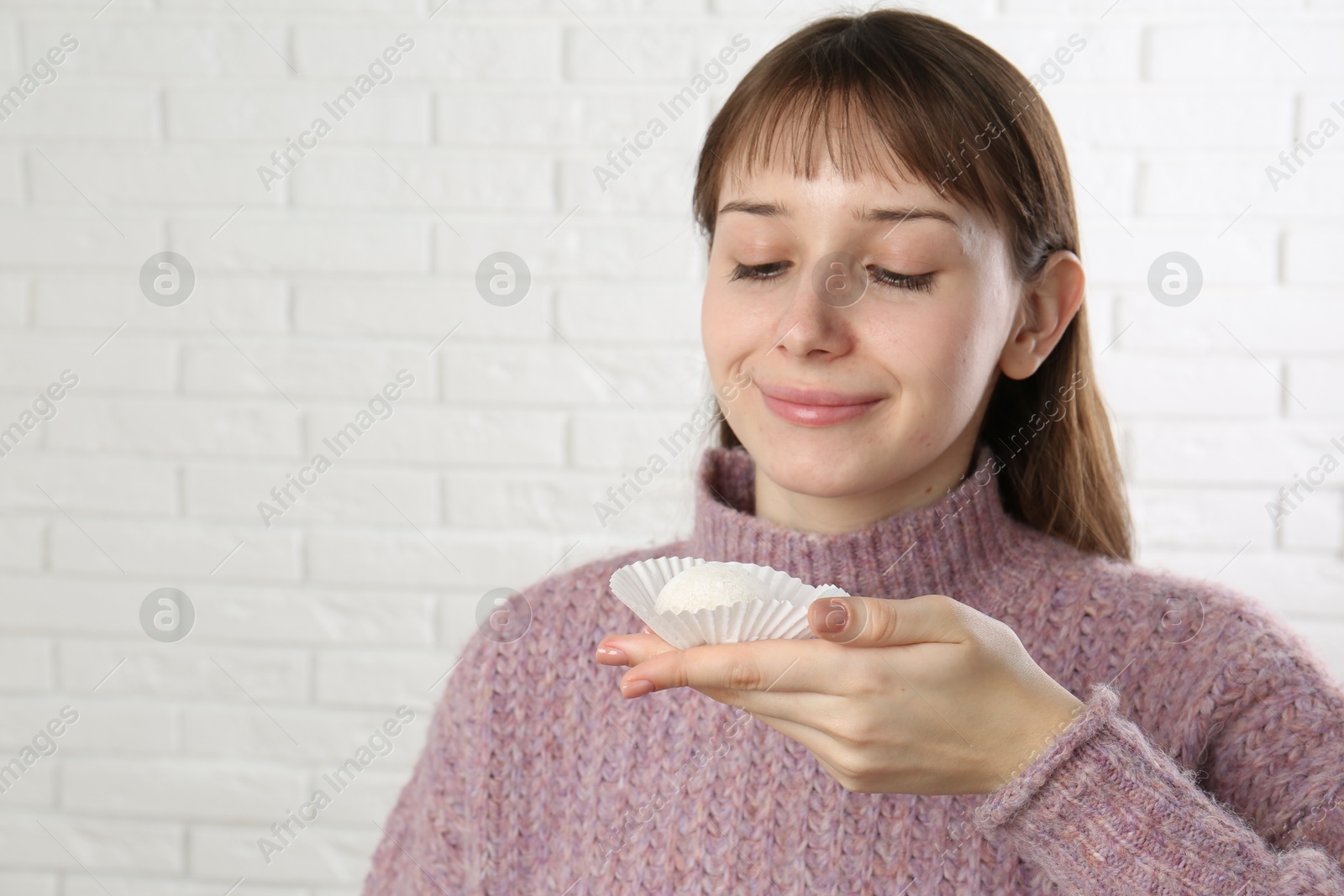 Photo of Beautiful woman with tasty mochi near white wall. Space for text