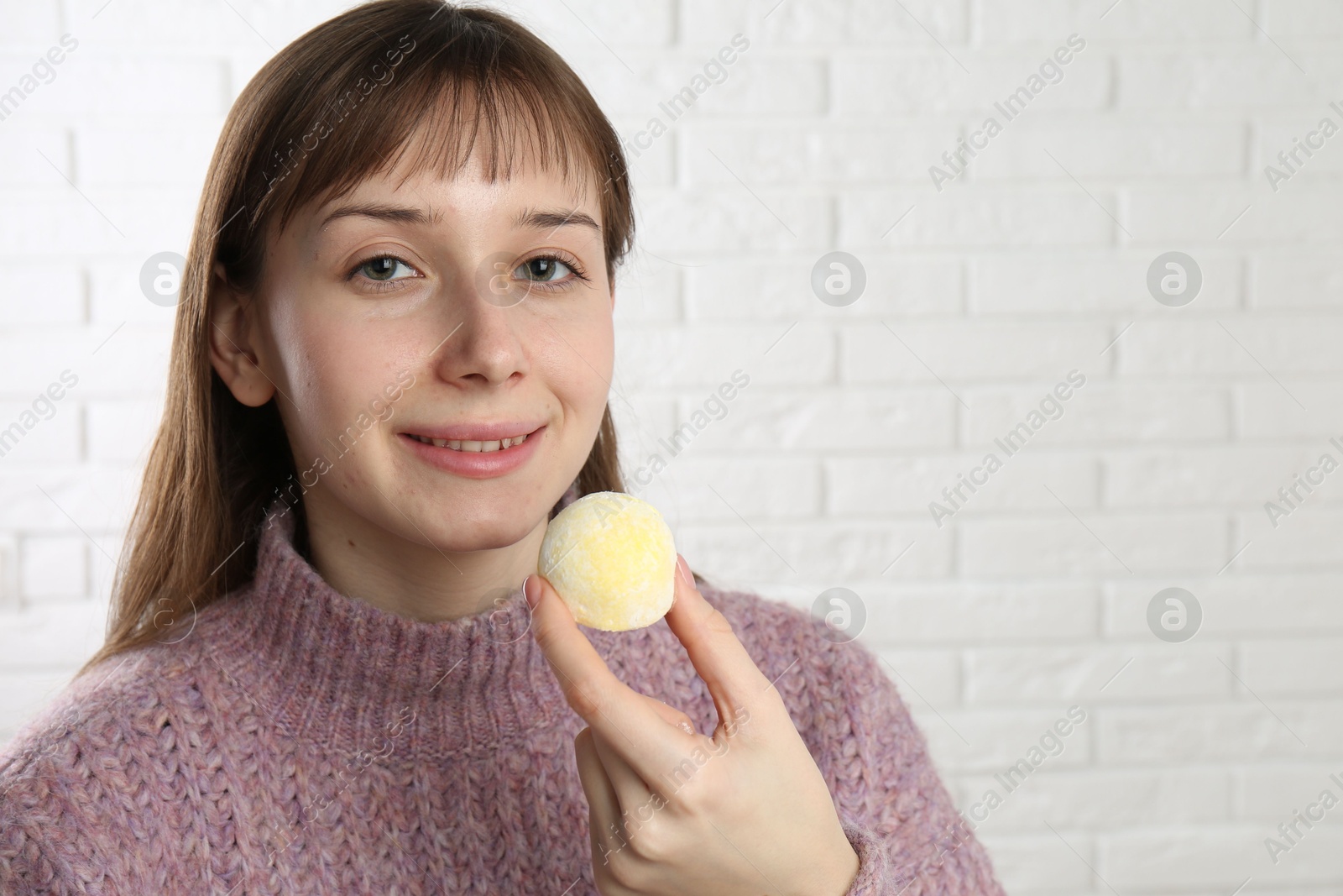 Photo of Smiling woman with tasty mochi near white wall. Space for text