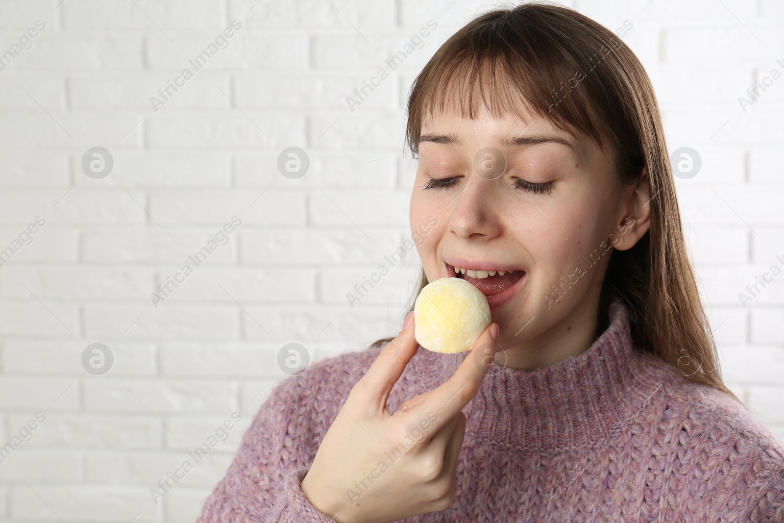 Photo of Beautiful woman eating tasty mochi near white wall. Space for text