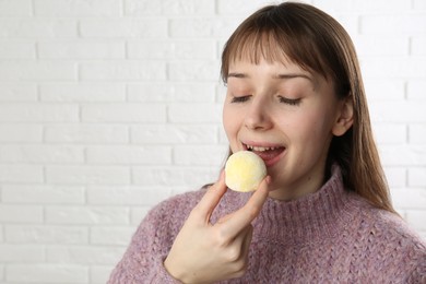 Photo of Beautiful woman eating tasty mochi near white wall. Space for text