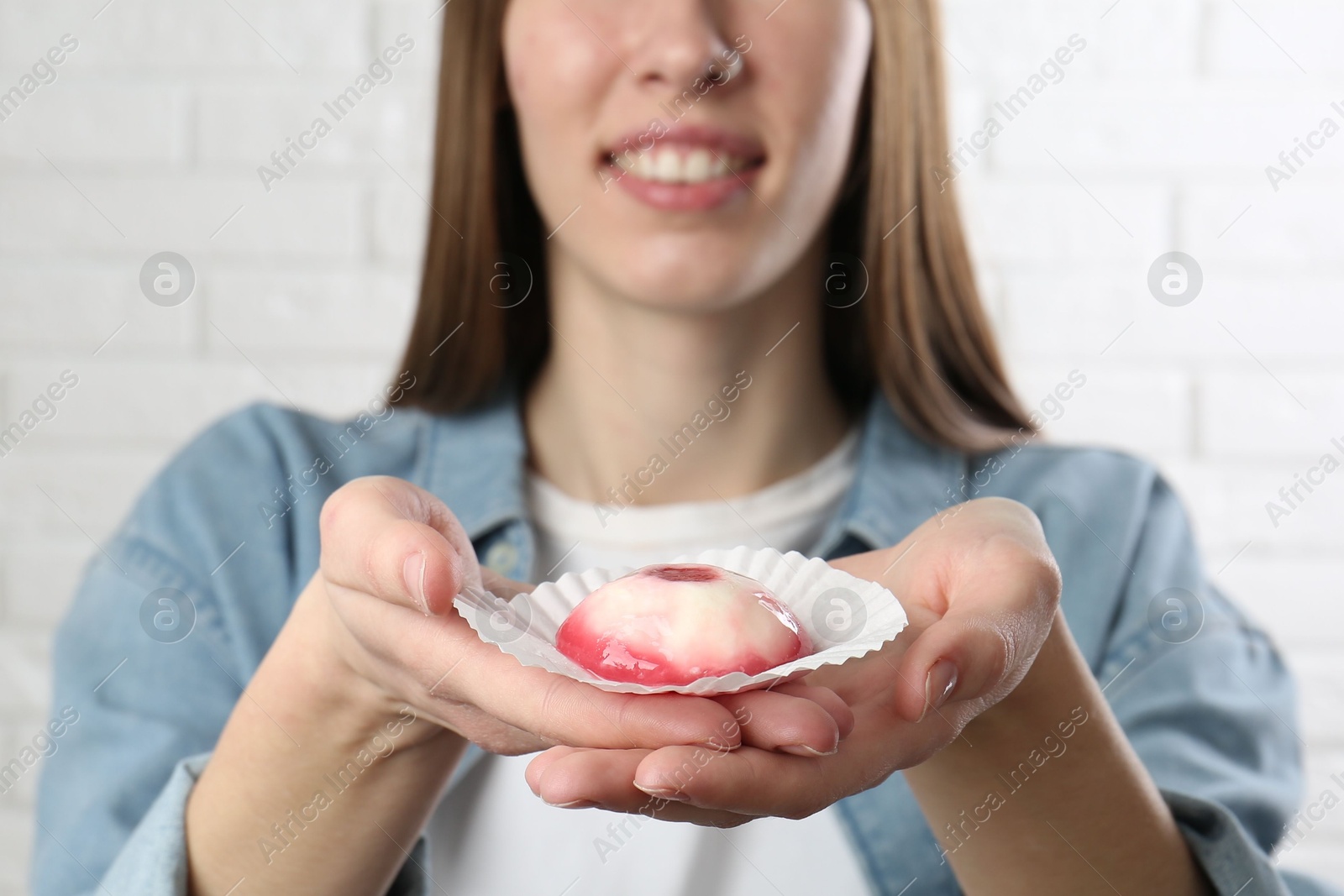 Photo of Smiling woman with tasty mochi near white wall, closeup