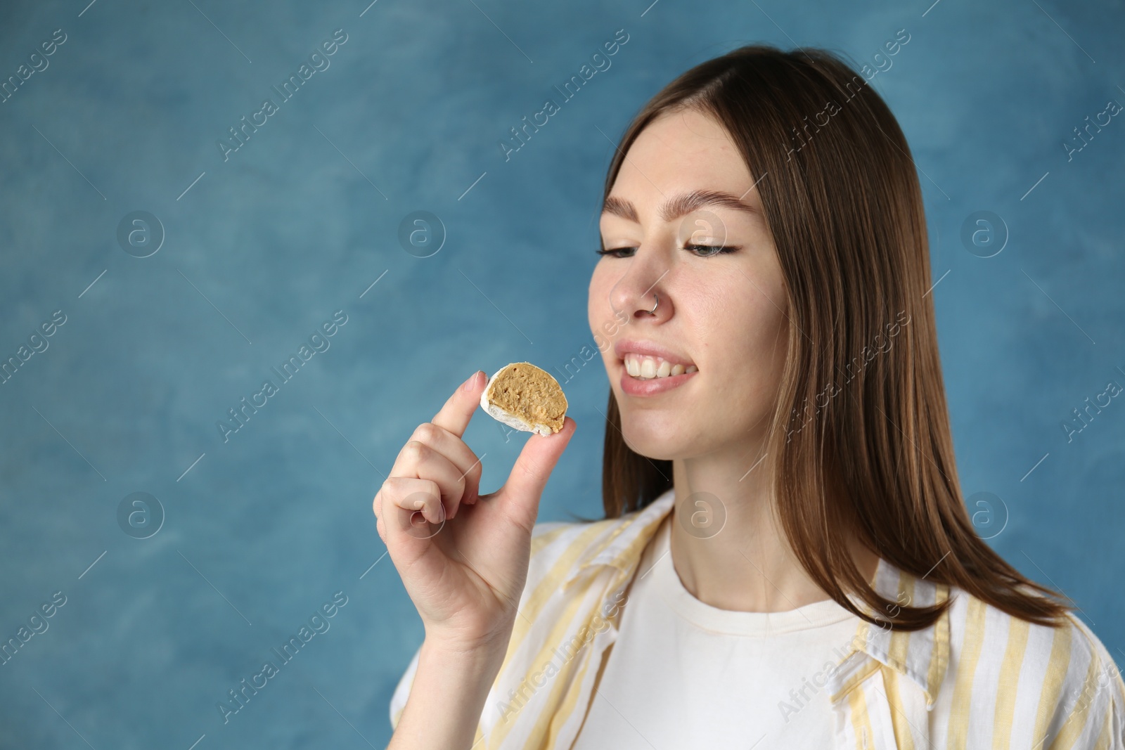 Photo of Beautiful woman eating tasty mochi on blurred blue background. Space for text