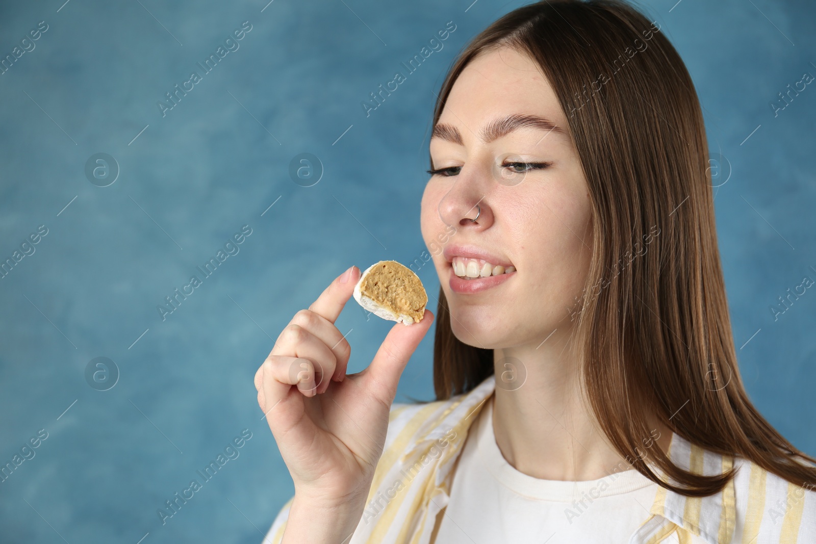 Photo of Beautiful woman eating tasty mochi on blurred blue background. Space for text