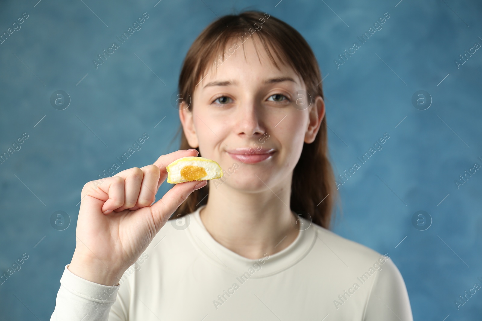 Photo of Beautiful woman with tasty mochi on blurred blue background, selective focus