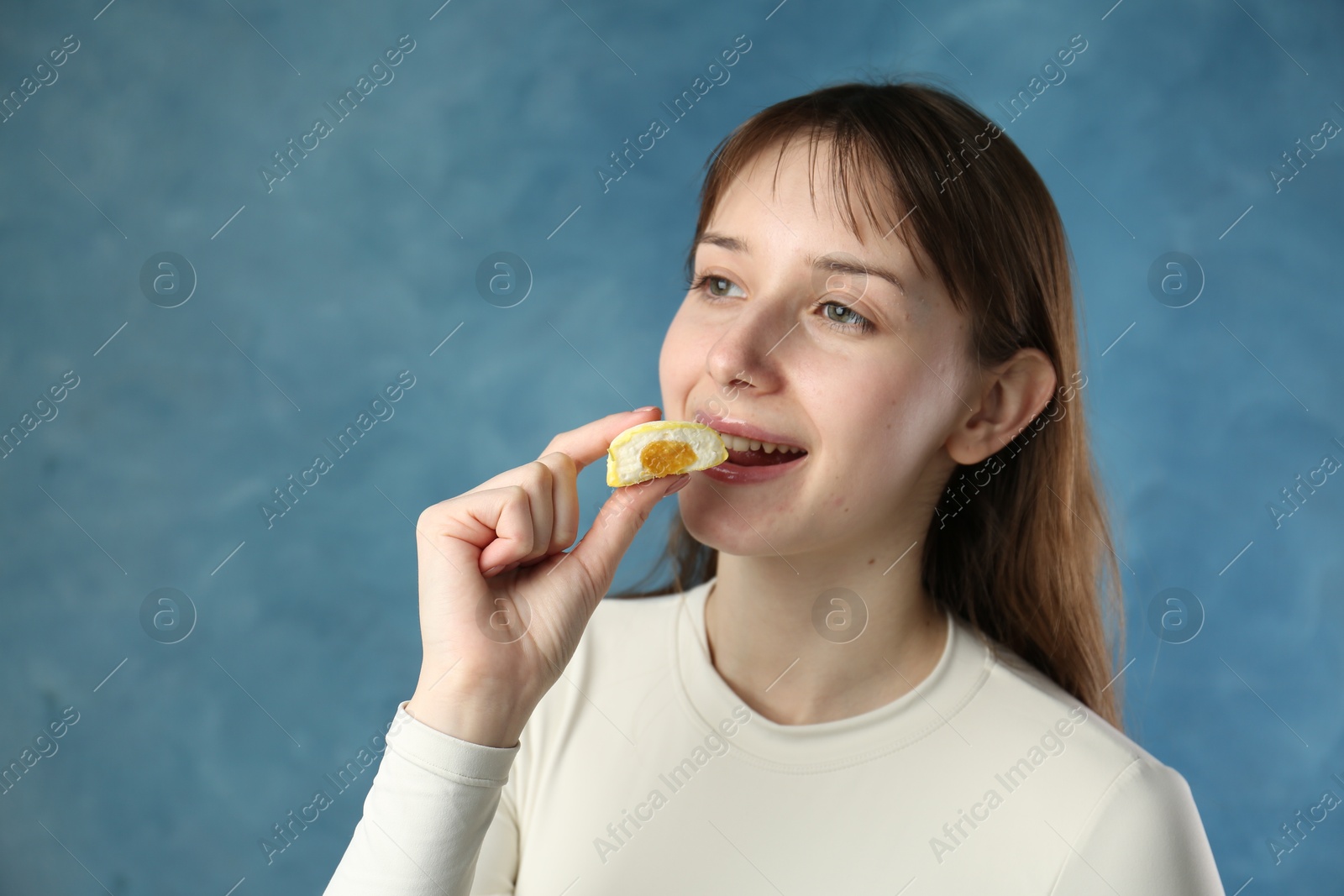 Photo of Beautiful woman eating tasty mochi on blurred blue background