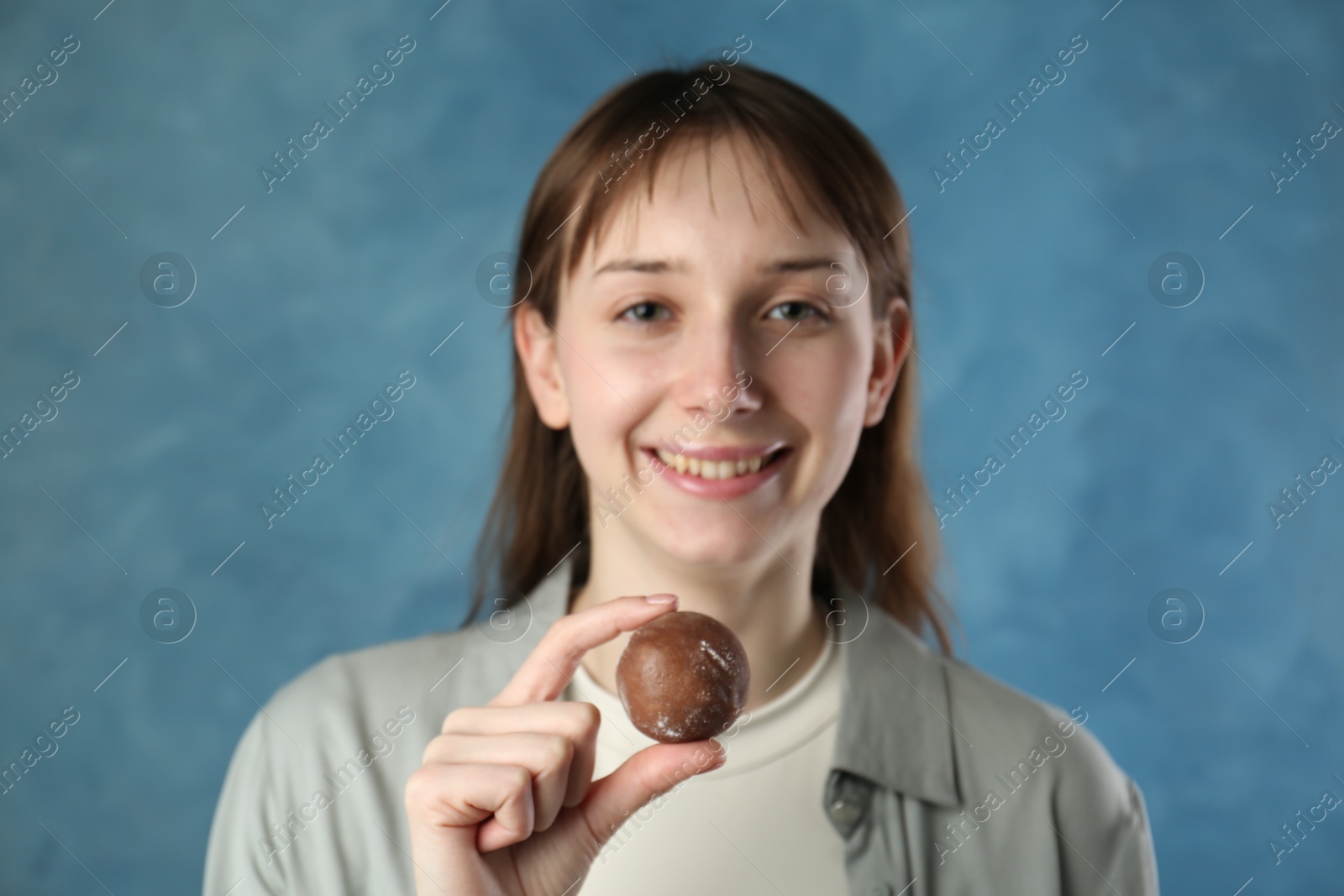 Photo of Smiling woman with tasty mochi on blurred blue background