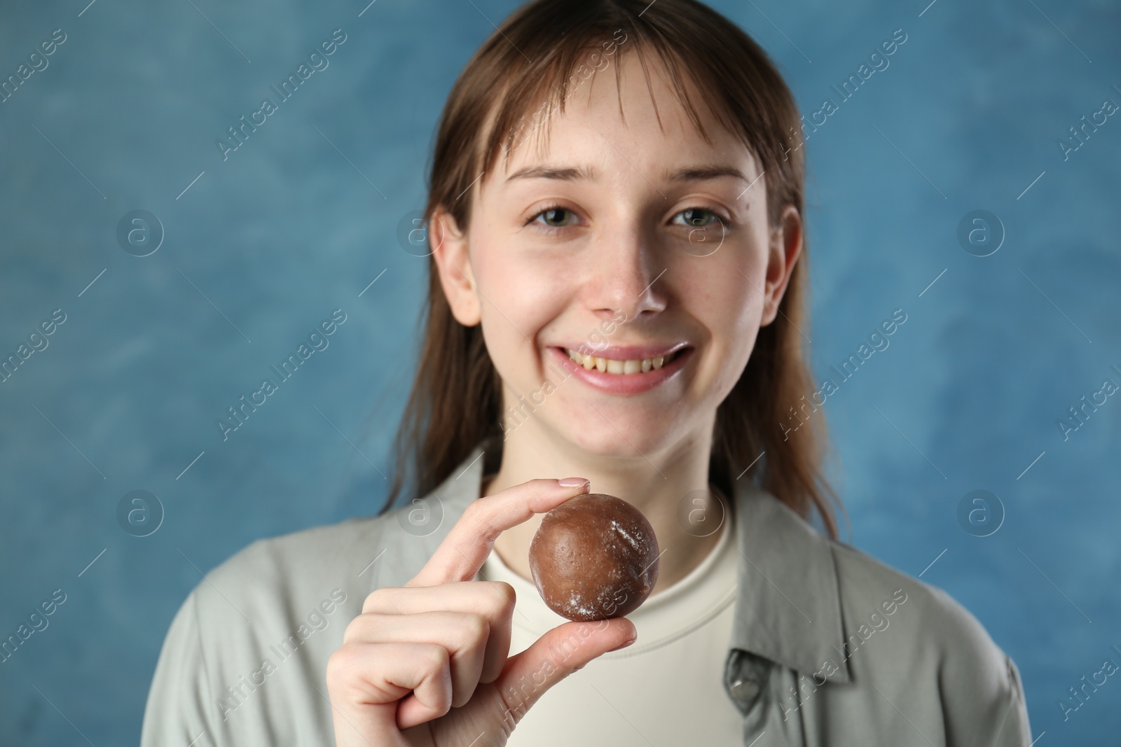 Photo of Smiling woman with tasty mochi on blurred blue background