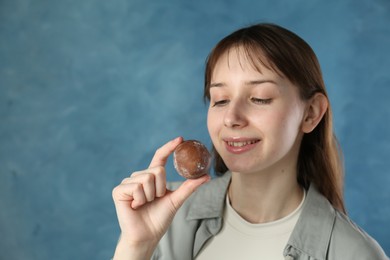 Photo of Smiling woman with tasty mochi on blurred blue background. Space for text