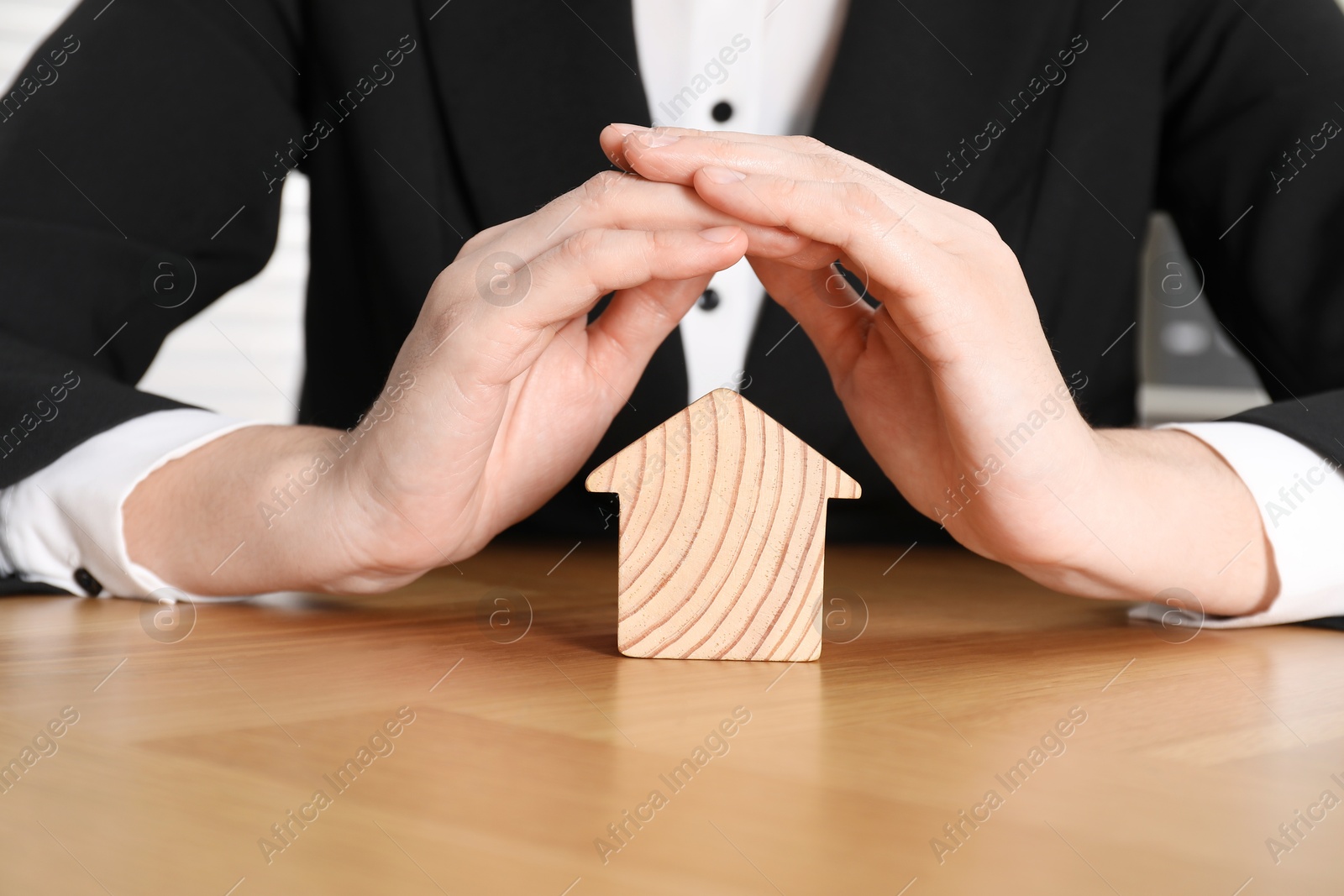 Photo of Property insurance. Real estate agent protecting wooden house figure at table indoors, closeup