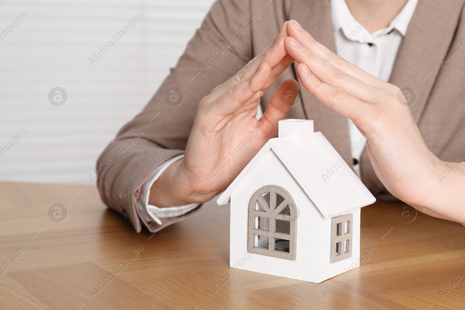 Photo of Property insurance. Real estate agent protecting house figure at wooden table indoors, closeup