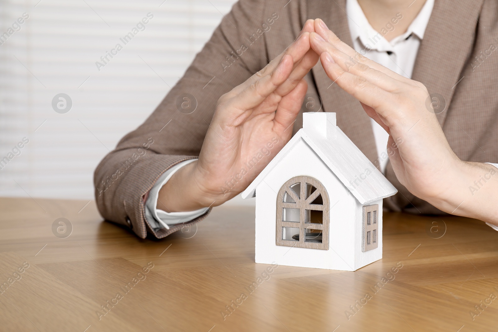 Photo of Property insurance. Real estate agent protecting house figure at wooden table indoors, closeup