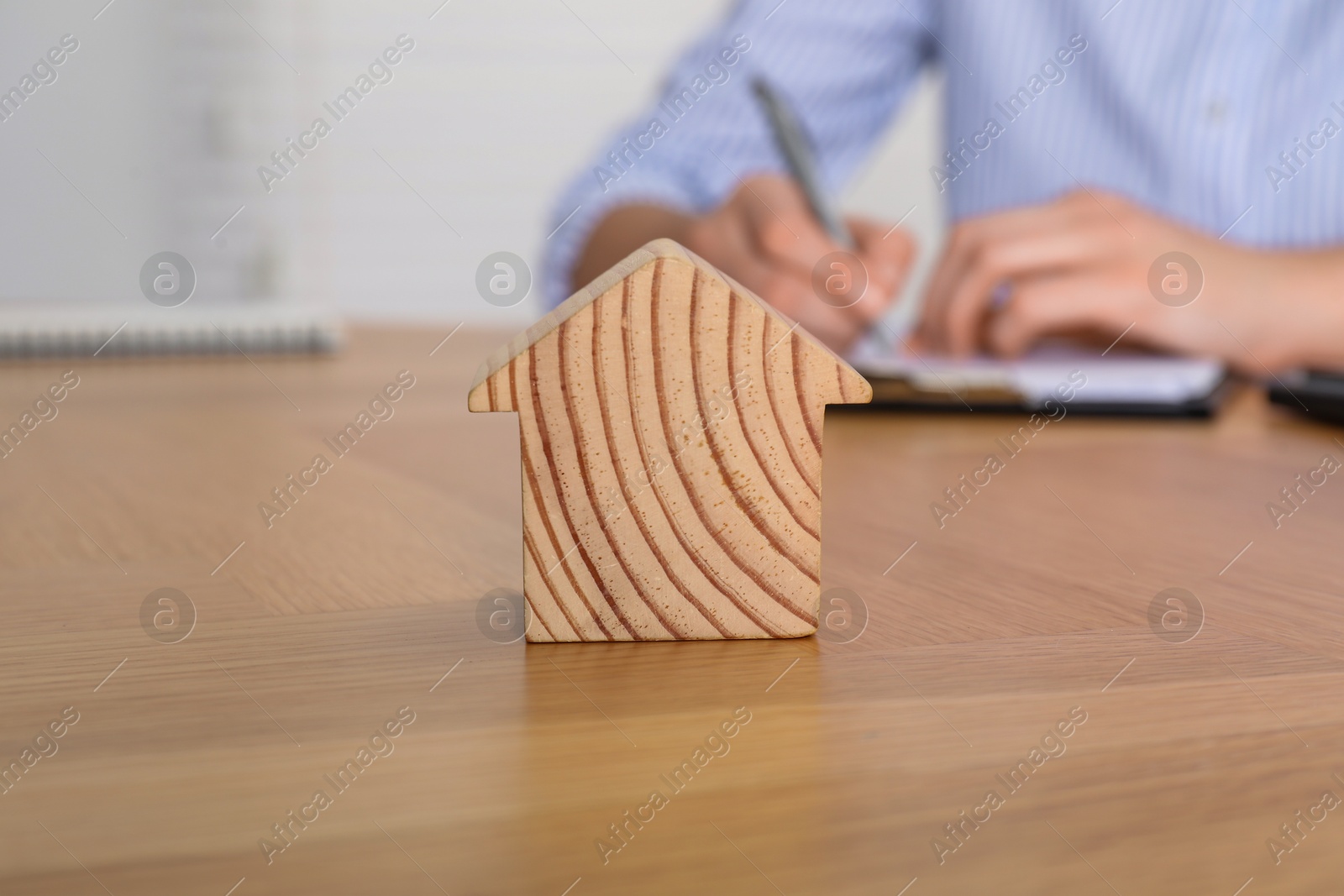 Photo of Property insurance. Real estate agent working at table indoors, focus on wooden house figure