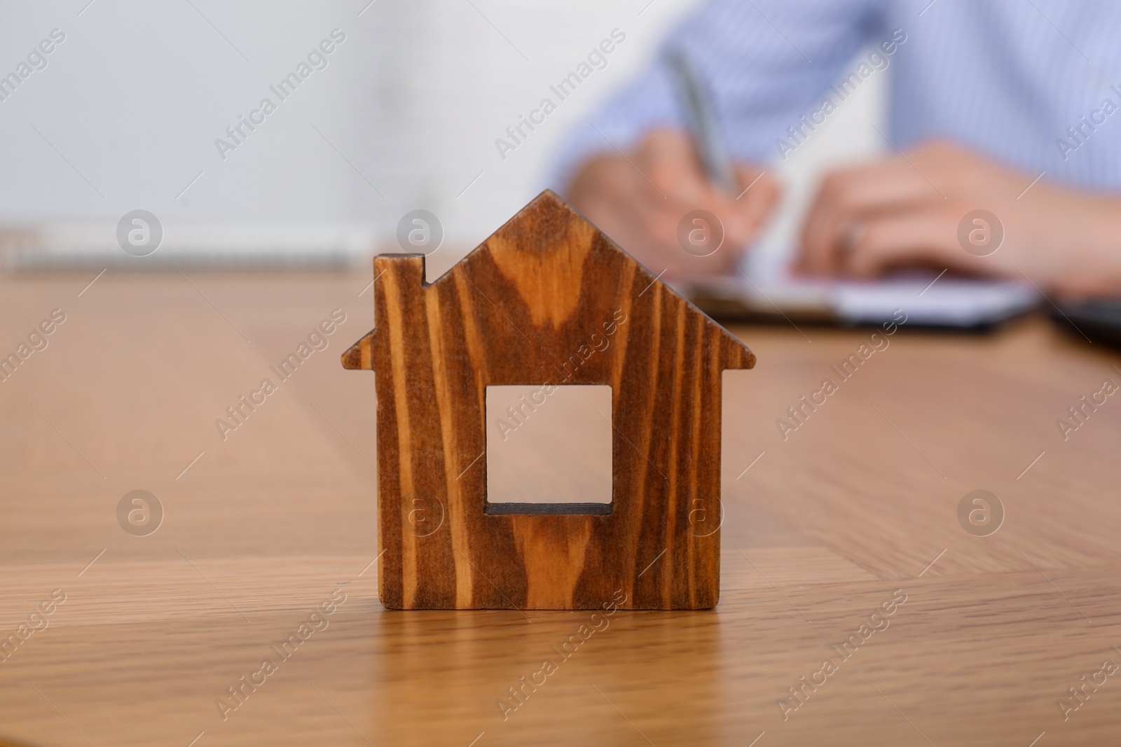 Photo of Property insurance. Real estate agent working at table indoors, focus on wooden house figure