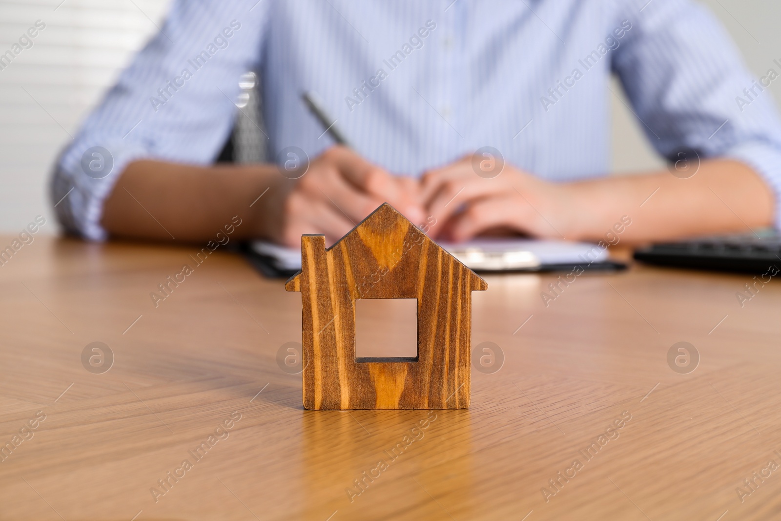 Photo of Property insurance. Real estate agent working at table indoors, focus on wooden house figure