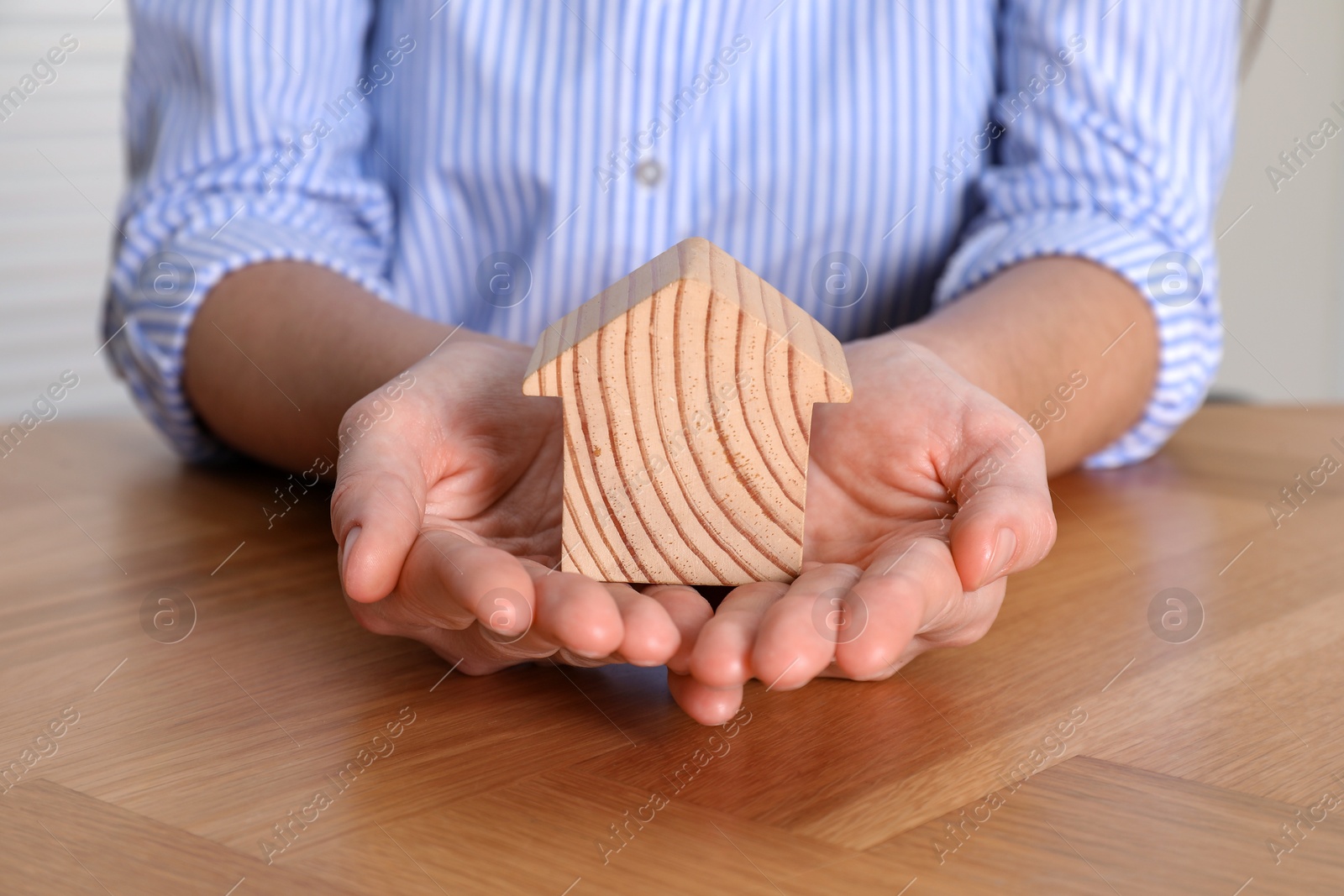 Photo of Property insurance. Real estate agent with wooden house figure at table indoors, closeup