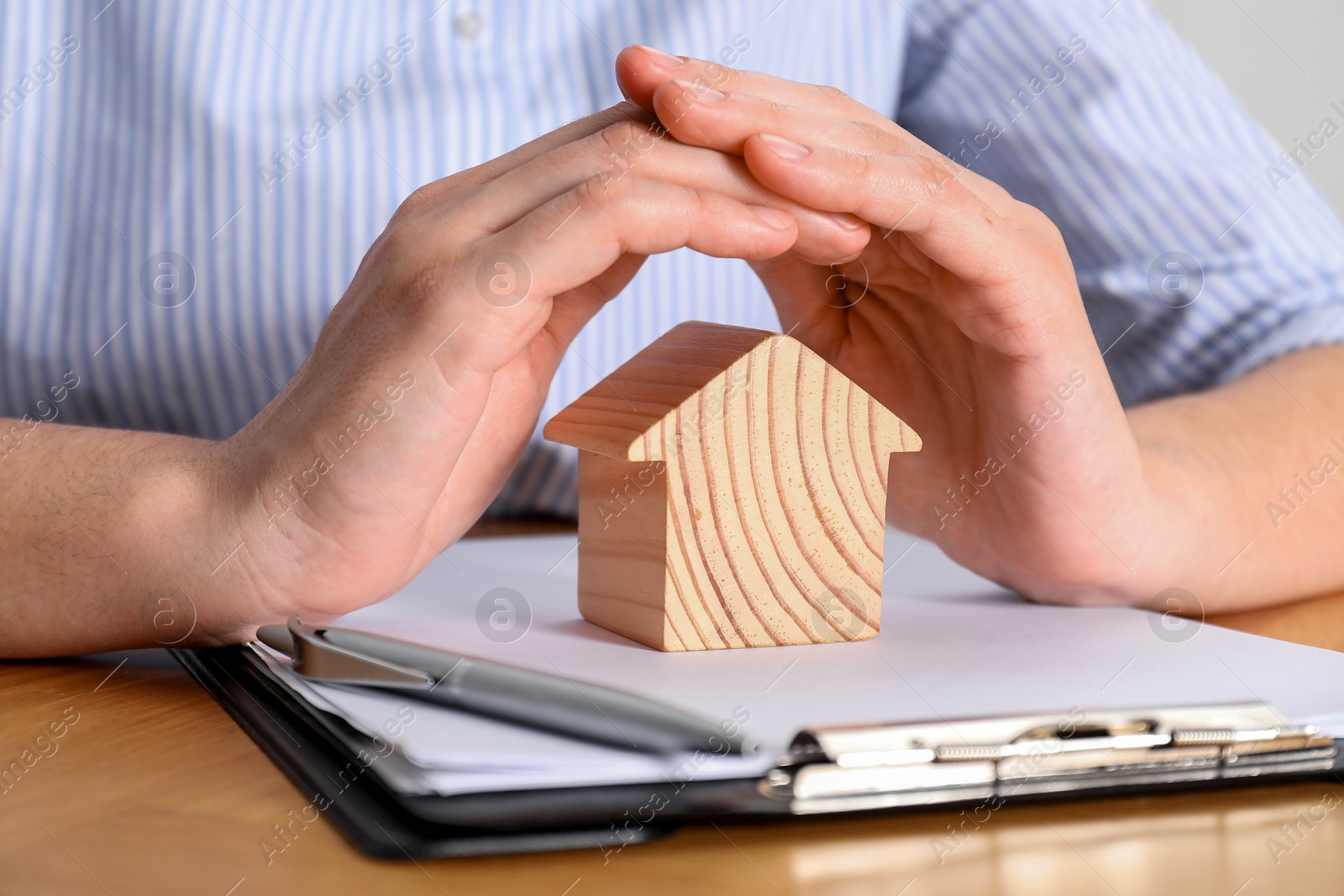 Photo of Property insurance. Real estate agent with wooden house figure at table indoors, closeup