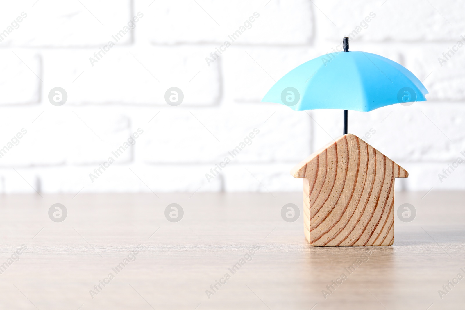 Photo of Property insurance. Wooden house figure and small umbrella on table indoors, space for text