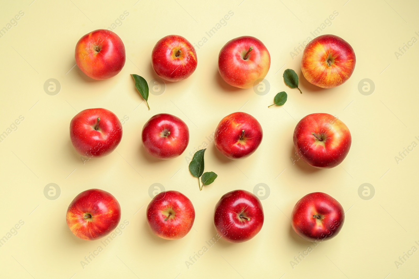 Photo of Many red apples and green leaves on beige background, flat lay