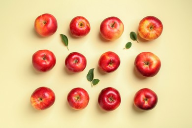 Many red apples and green leaves on beige background, flat lay