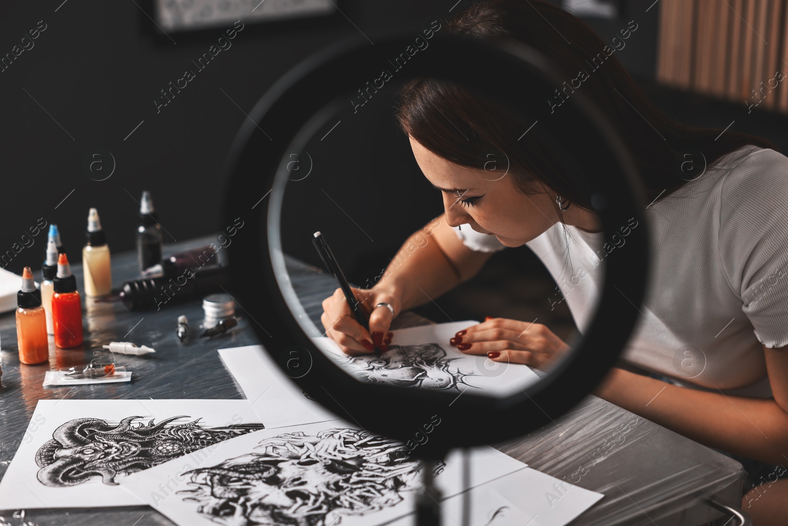 Photo of Tattoo artist drawing sketch at table with supplies in salon