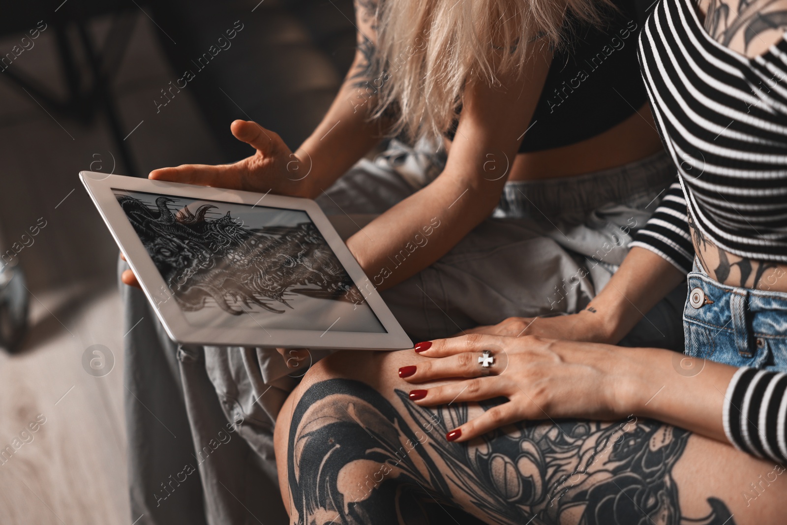 Photo of Tattoo artist showing tablet with sketch to client in salon, closeup