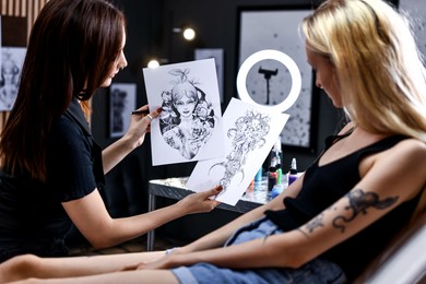 Photo of Tattoo artist showing different sketches to client in salon