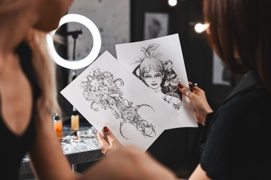 Photo of Tattoo artist showing different sketches to client in salon, closeup