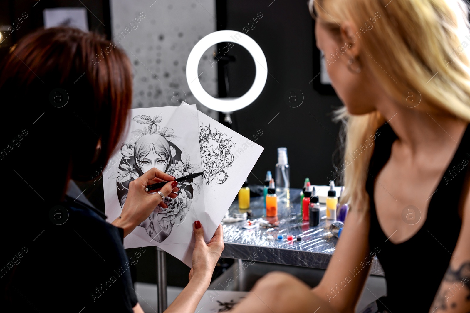 Photo of Tattoo artist showing different sketches to client in salon