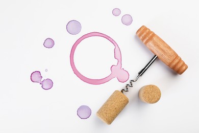 Corkscrew, cork and red wine stains on white background, top view