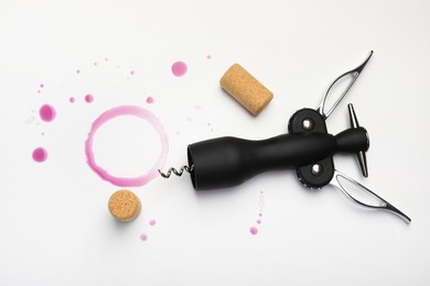 Photo of Wing corkscrew, corks and red wine stains on white background, top view