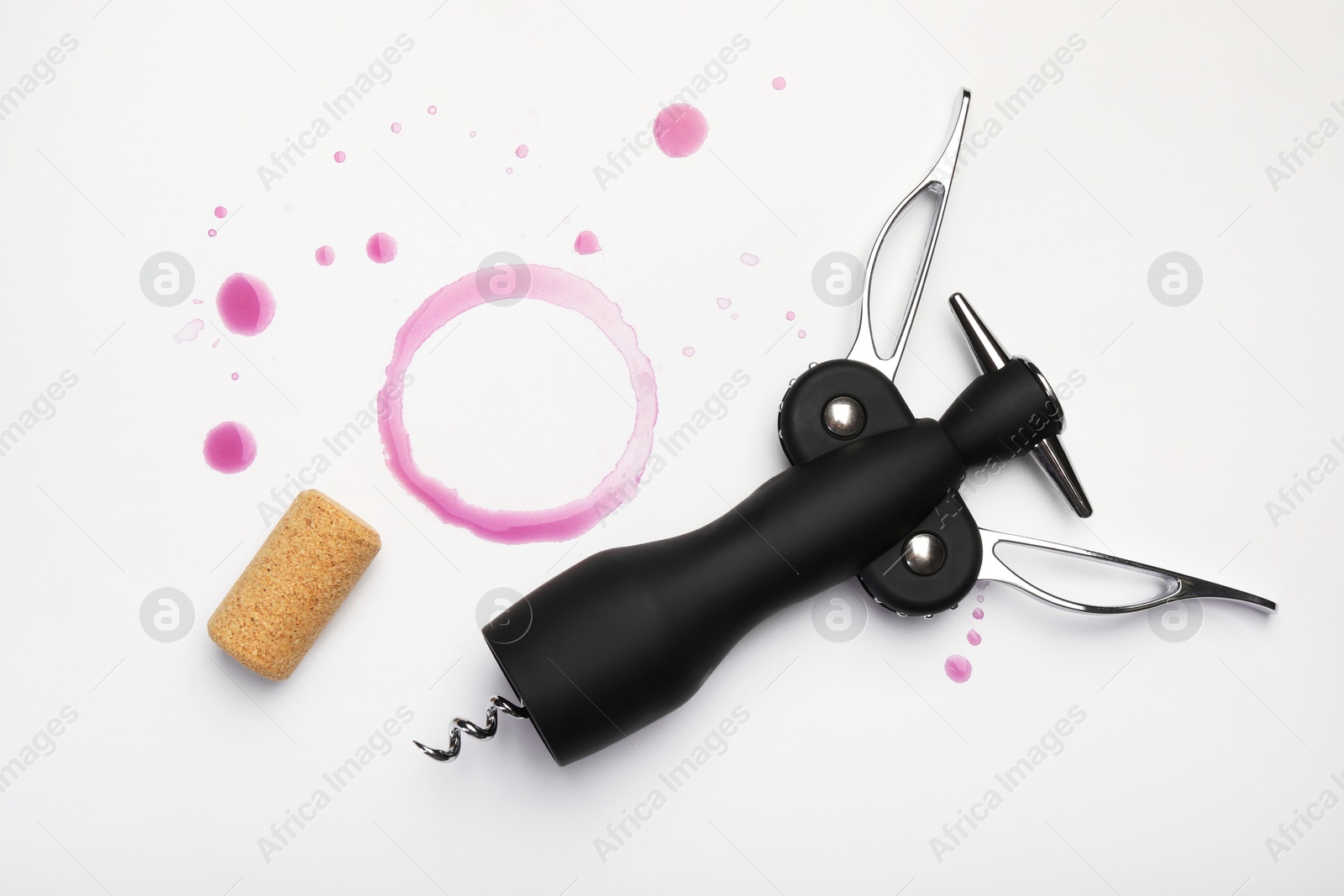 Photo of Wing corkscrew, cork and red wine stains on white background, top view