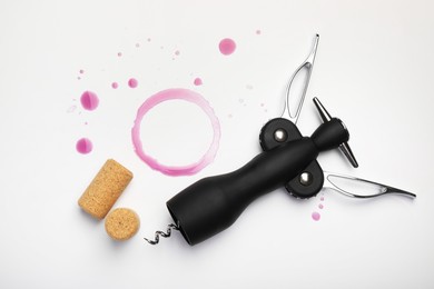 Wing corkscrew, corks and red wine stains on white background, top view