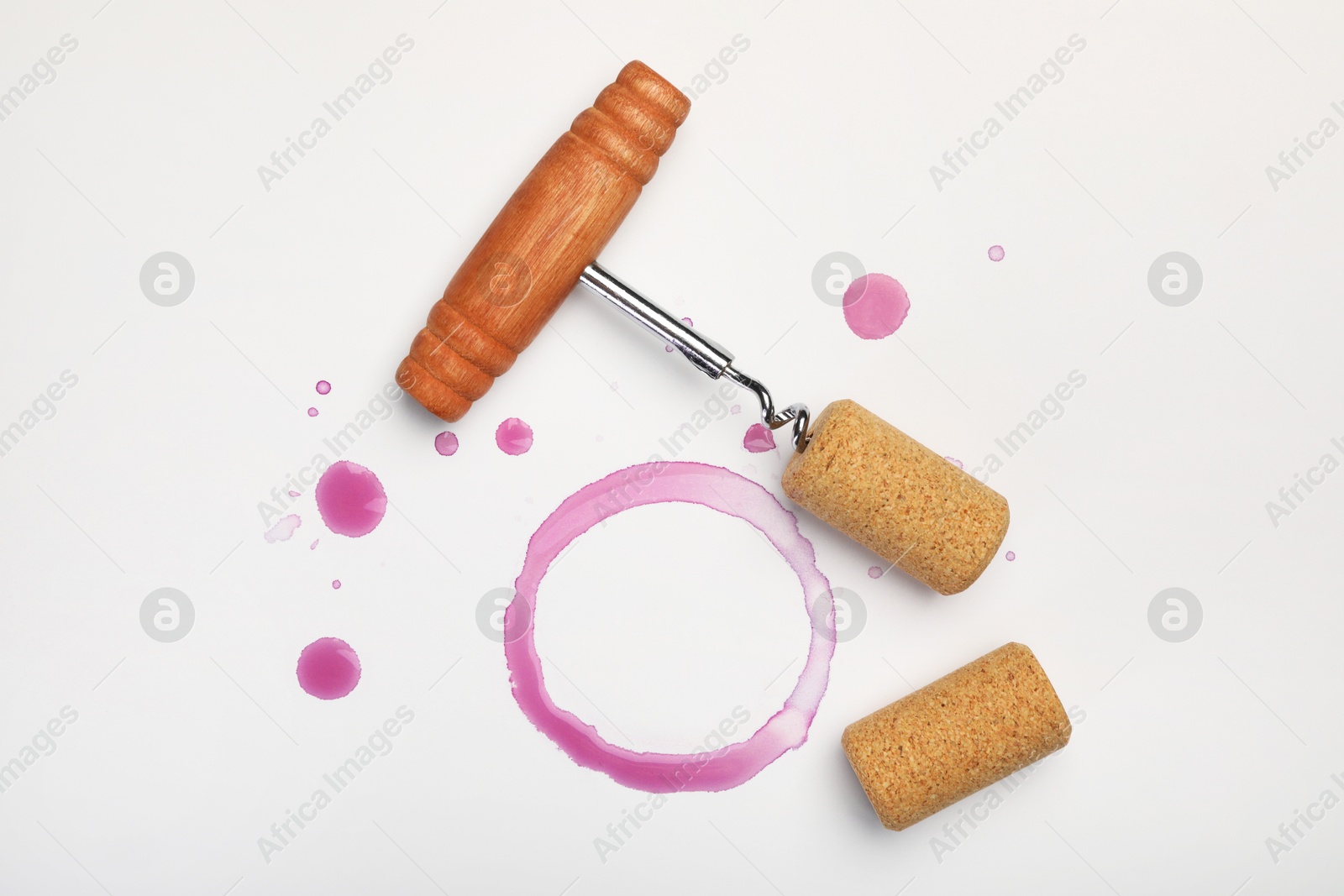 Photo of Corkscrew, corks and red wine stains on white background, top view