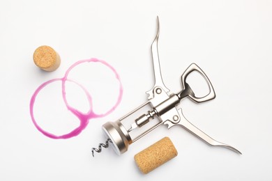 Photo of Wing corkscrew, corks and red wine stains on white background, top view