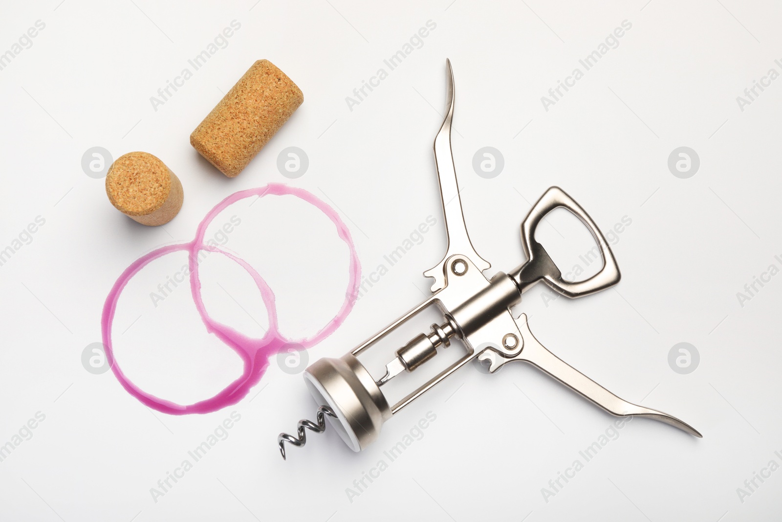 Photo of Wing corkscrew, corks and red wine stains on white background, top view