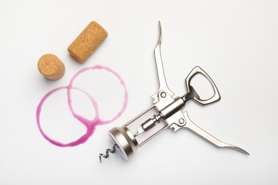 Photo of Wing corkscrew, corks and red wine stains on white background, top view