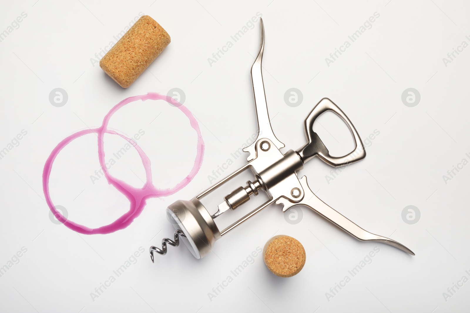 Photo of Wing corkscrew, corks and red wine stains on white background, top view