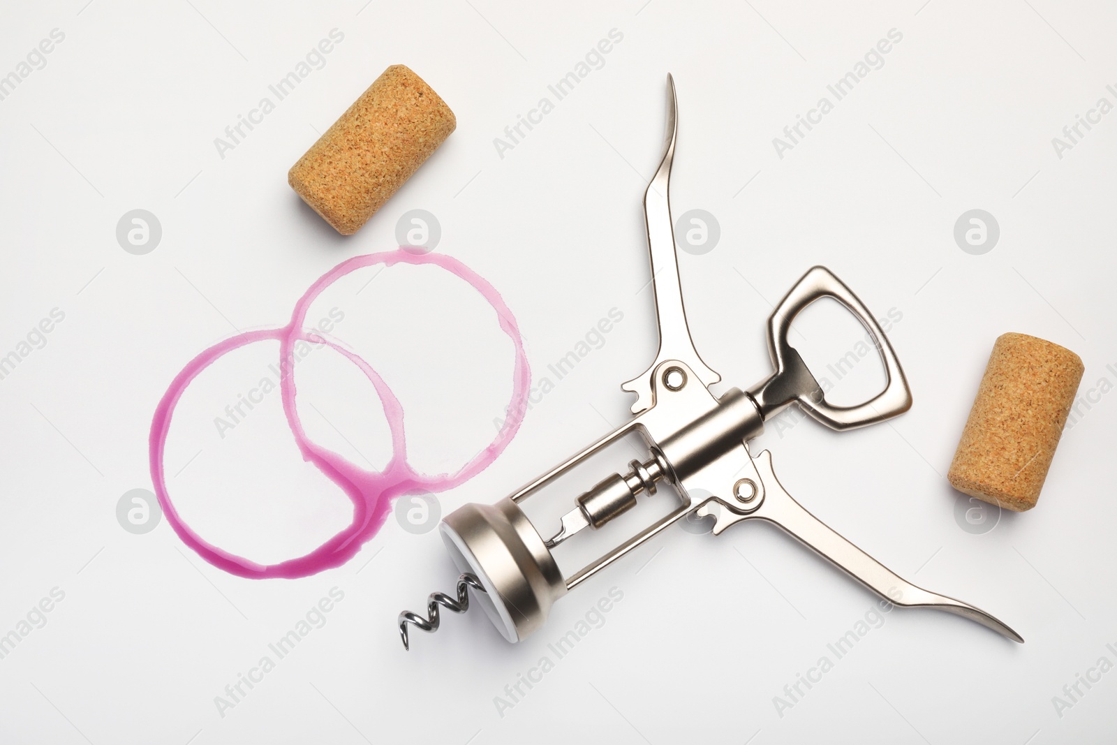 Photo of Wing corkscrew, corks and red wine stains on white background, top view