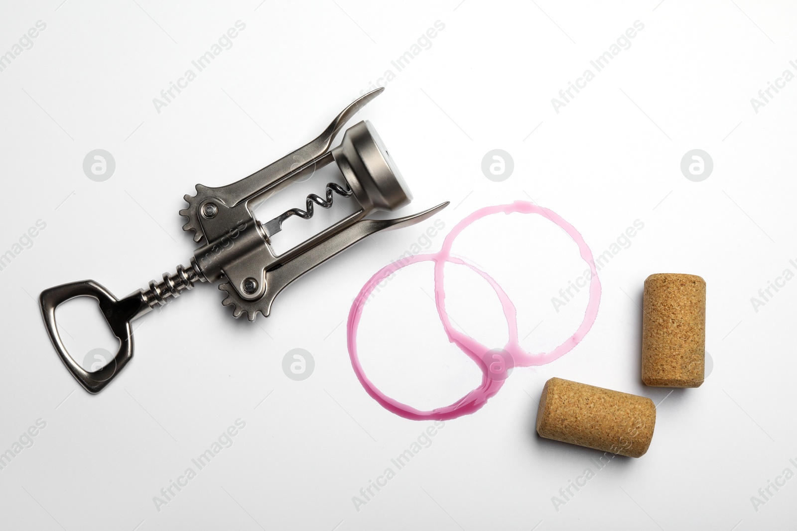 Photo of Wing corkscrew, corks and red wine stains on white background, top view